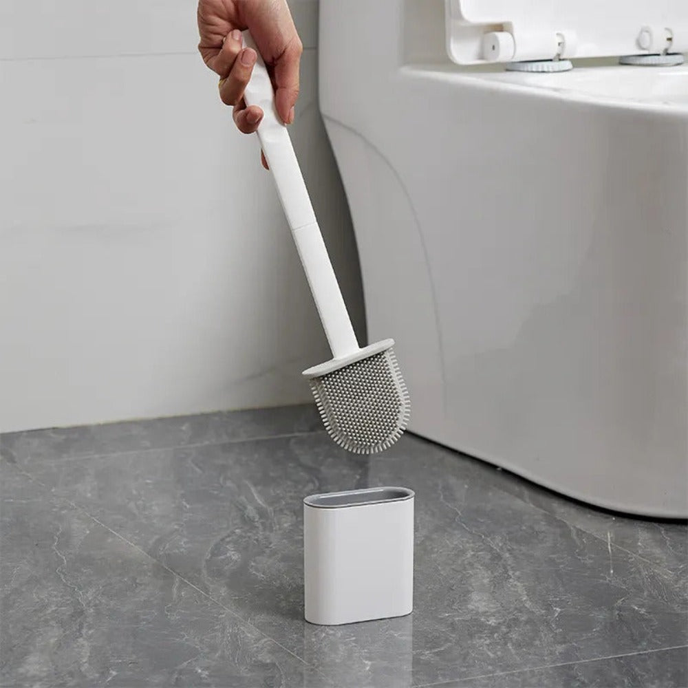 Person using a white toilet brush with a holder on a gray floor next to a white toilet.