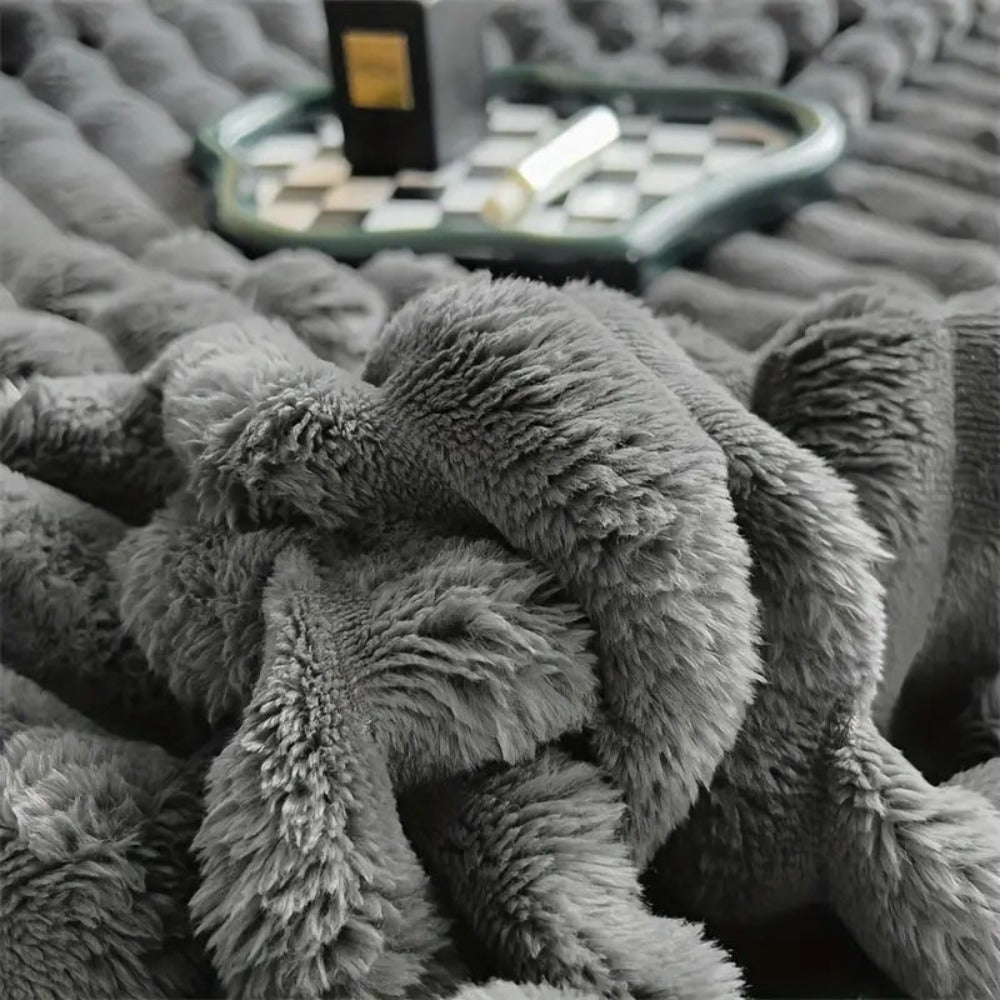 Gray plush blanket on a textured surface with a tray and items in the background