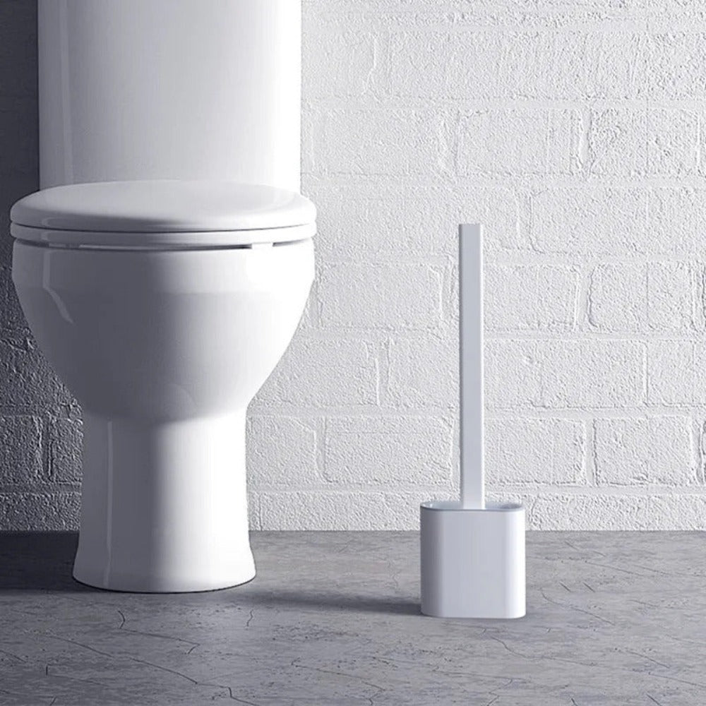 White toilet with a brush against a white brick wall