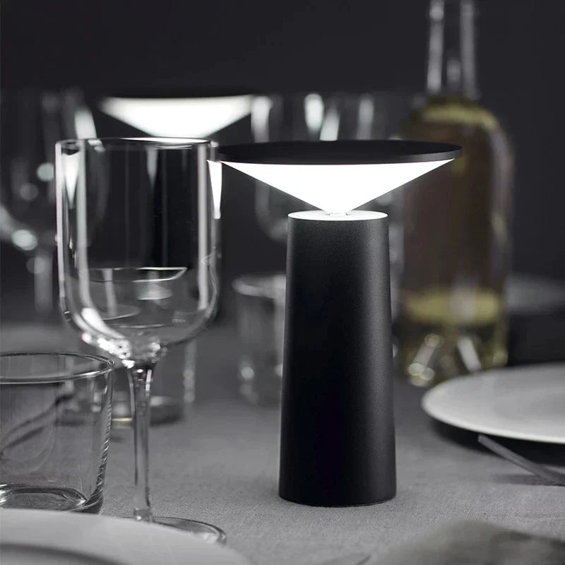 Modern black table lamp on a dining table with glasses and plates.