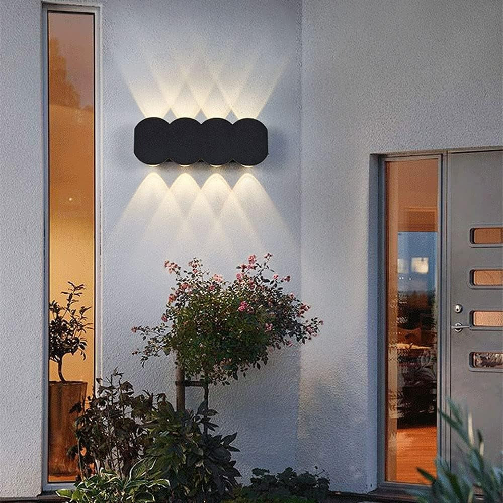 Modern outdoor wall light fixture on a building exterior with plants and a door.
