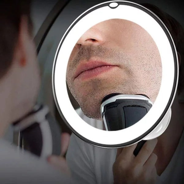 Person using a handheld mirror with a lighted ring to shave.