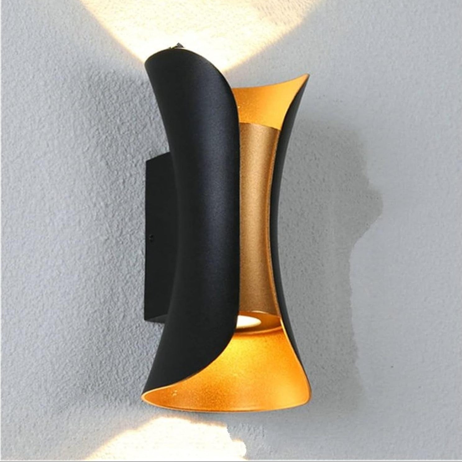 Modern wall light fixture with black and gold design on a gray wall.