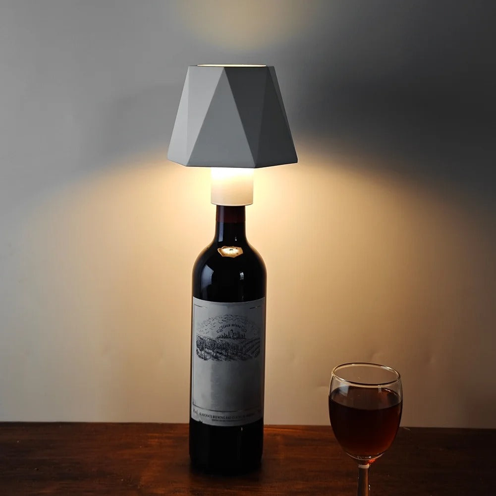 Wine bottle with geometric lampshade and glass of red wine on a wooden surface.