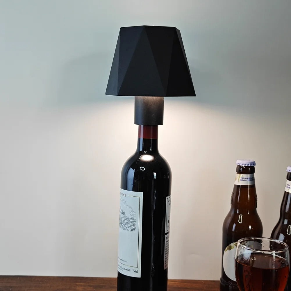 Black lampshade on a wine bottle with beer bottles and a glass in the background