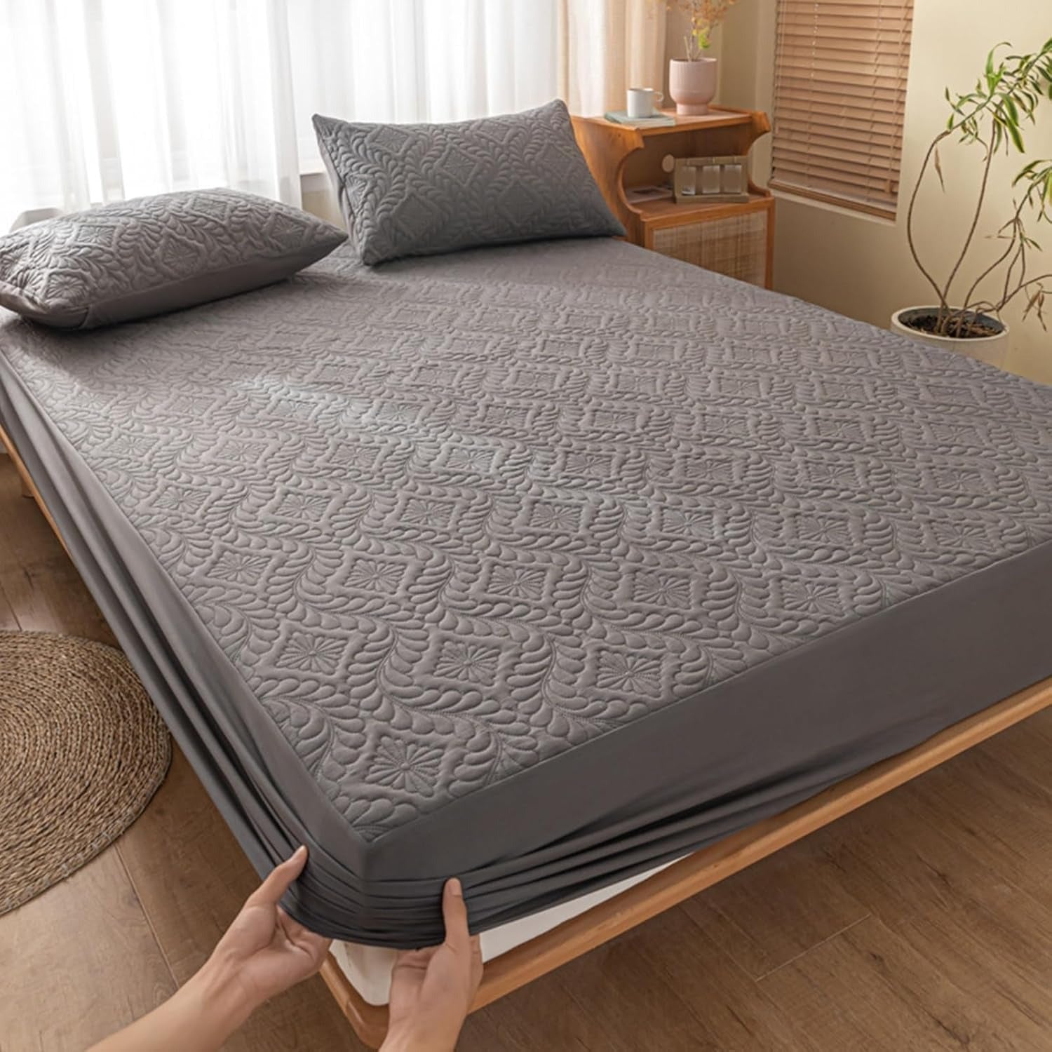 Person holding a gray mattress cover over a bed in a bedroom.