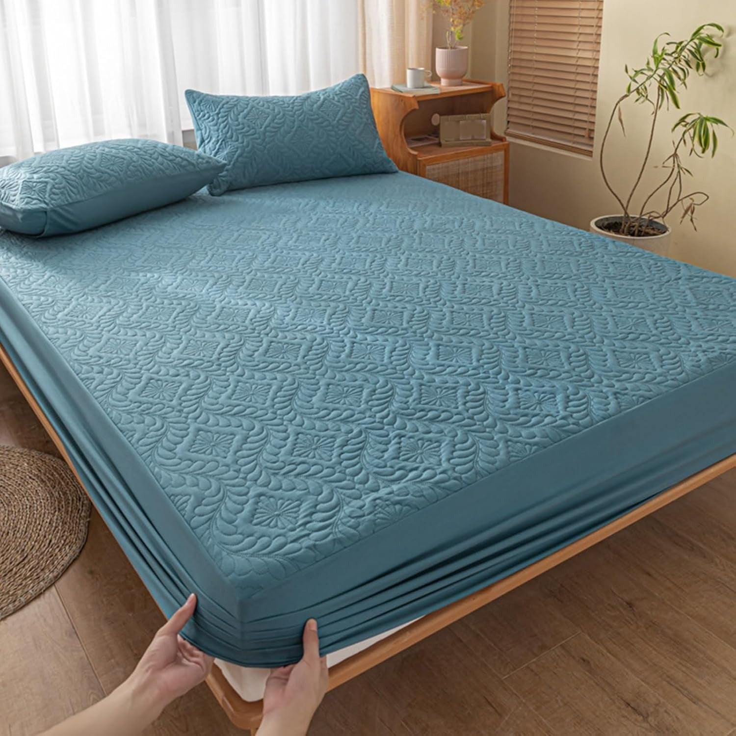 Blue textured mattress cover being fitted onto a bed in a bedroom.