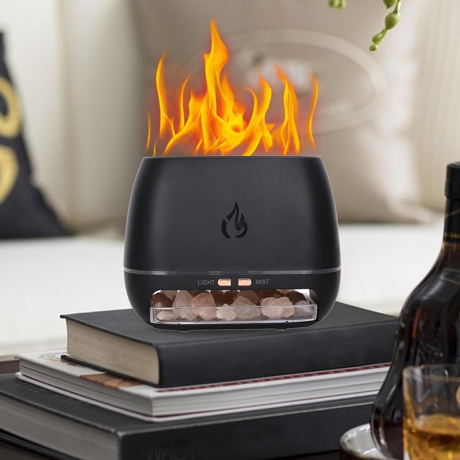 Black flame-shaped device with flames on a table with books and a bottle.