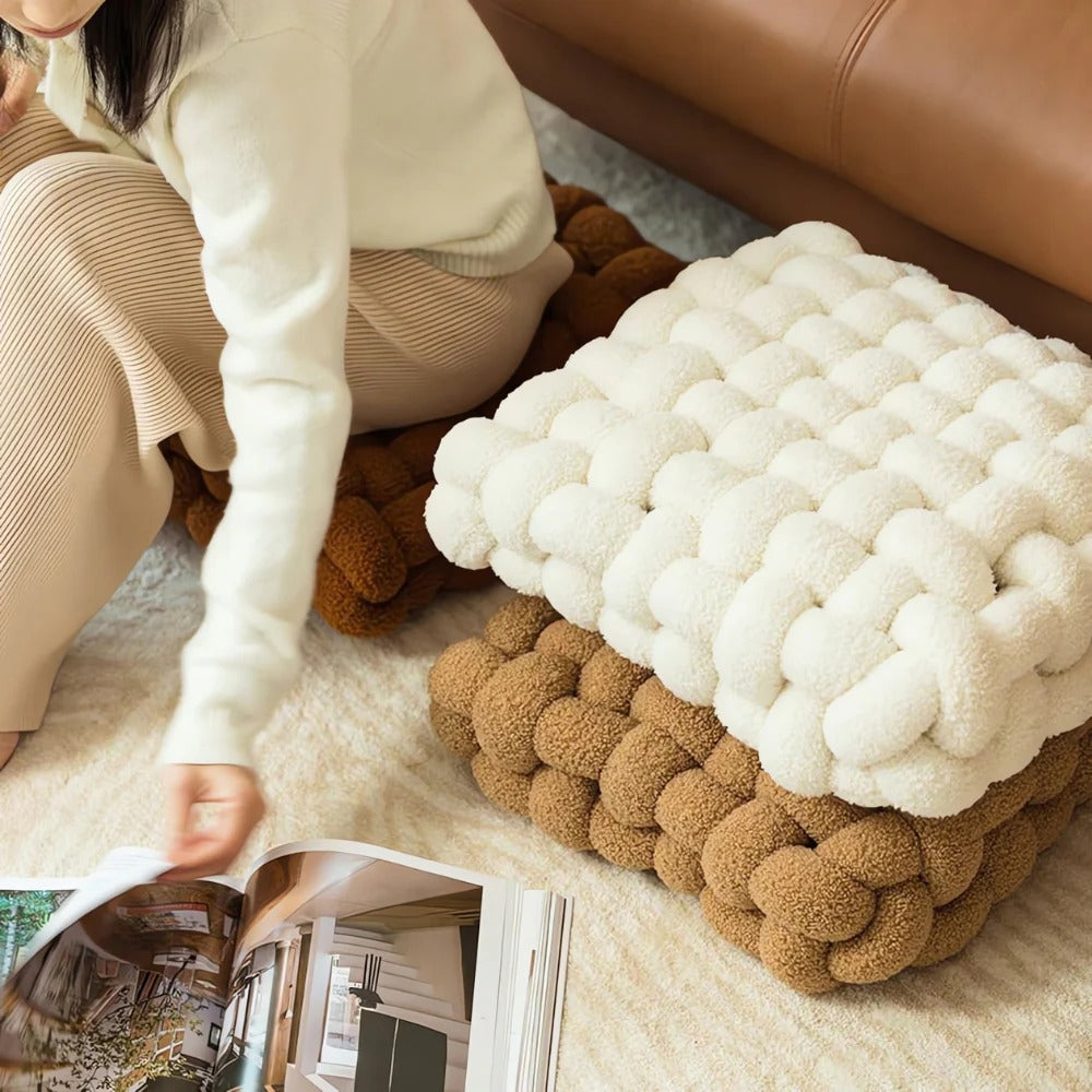 Two braided ottomans, one white and one brown, on a carpeted floor with a person reading a magazine.