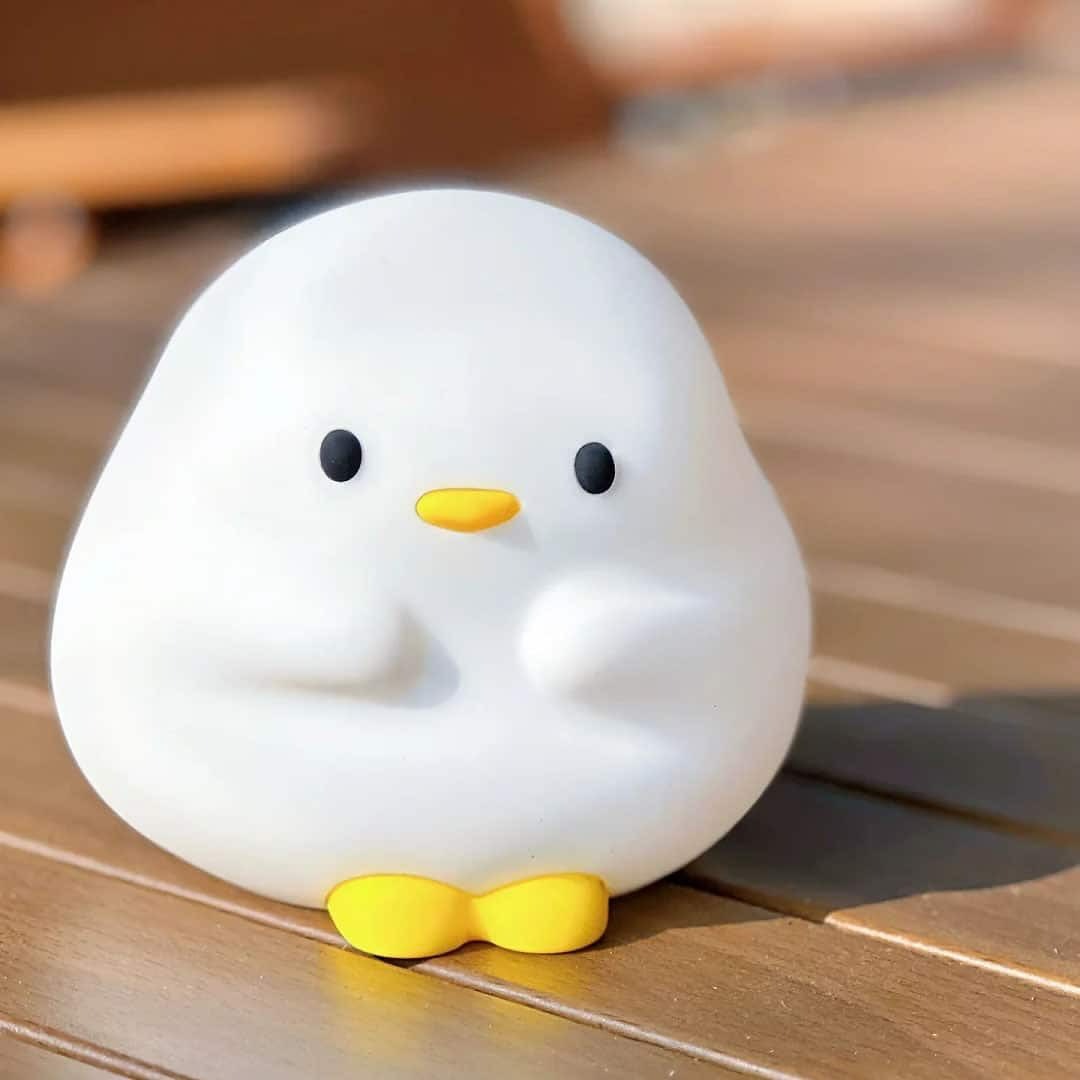 White duck-shaped object with a yellow bow tie on a wooden surface