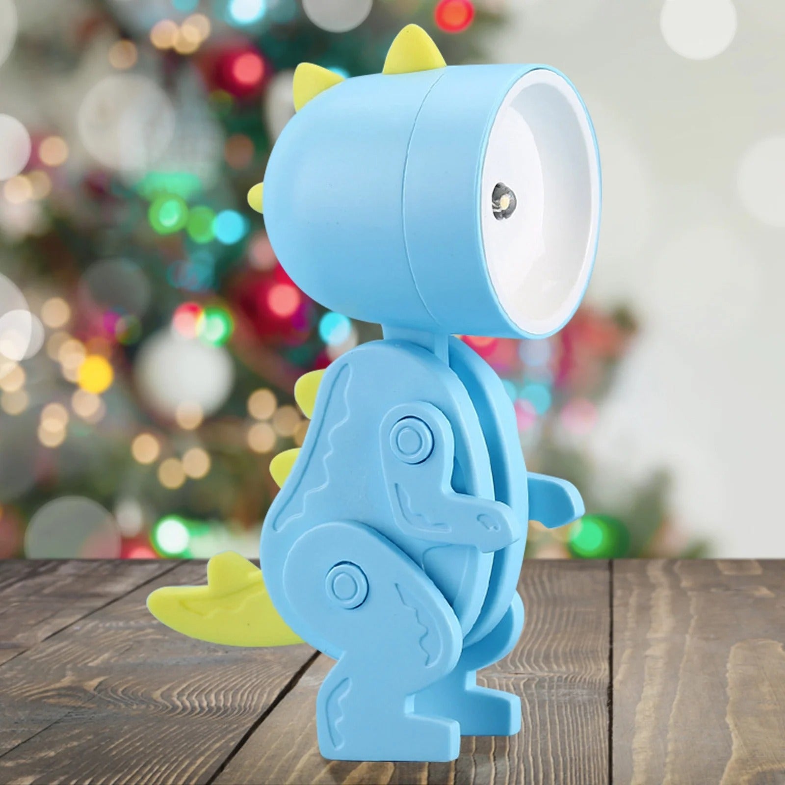Blue dinosaur-shaped lamp on a wooden surface with a blurred festive background