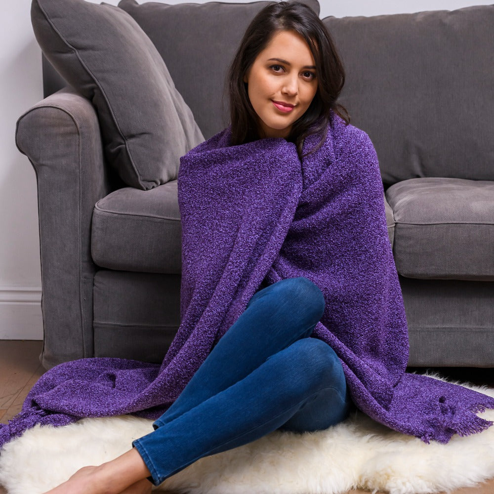 Woman sitting on a rug with a purple blanket wrapped around her, in front of a gray couch.