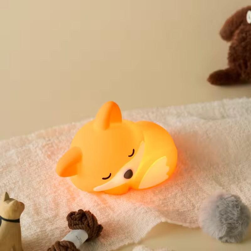 Fox-shaped night light on a soft surface with plush toys around