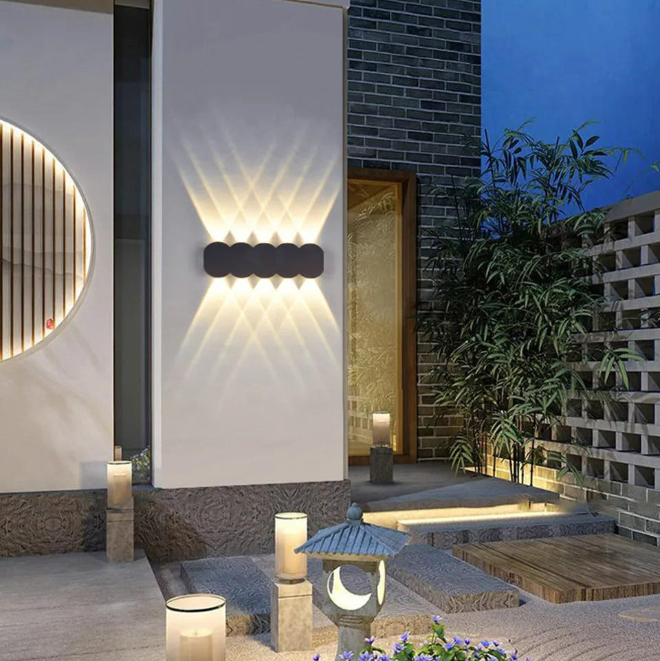 Modern outdoor setting with wall lights, candles, and a small pond.