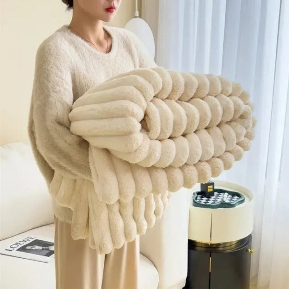 Person holding a large beige knitted blanket in a living room setting.