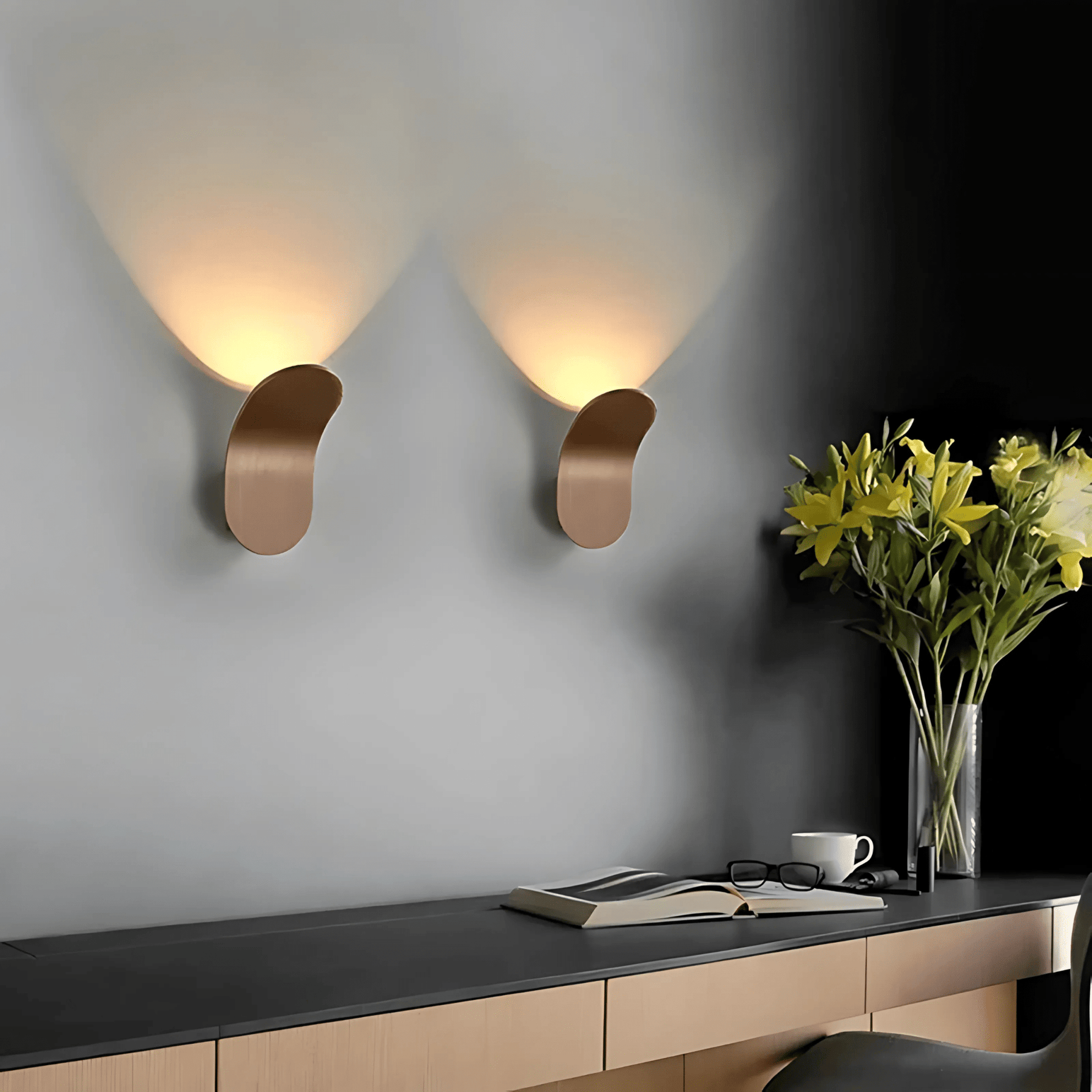 Modern wall sconces on a gray wall with a vase of flowers and a desk.