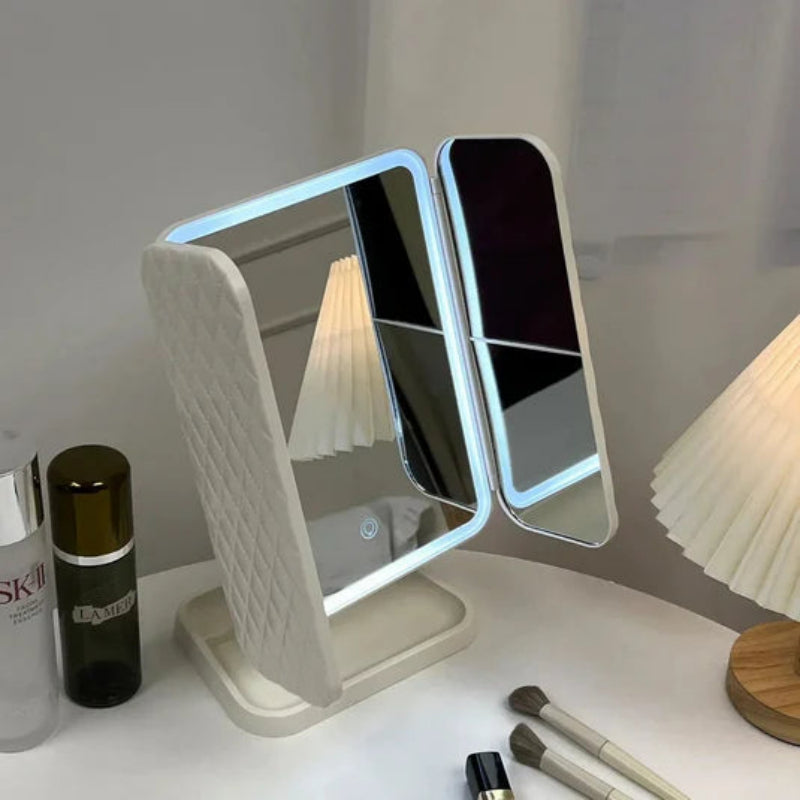 Lighted makeup mirror on a desk with skincare products and brushes.