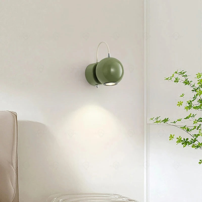Green wall lamp on a white wall with a plant in the corner