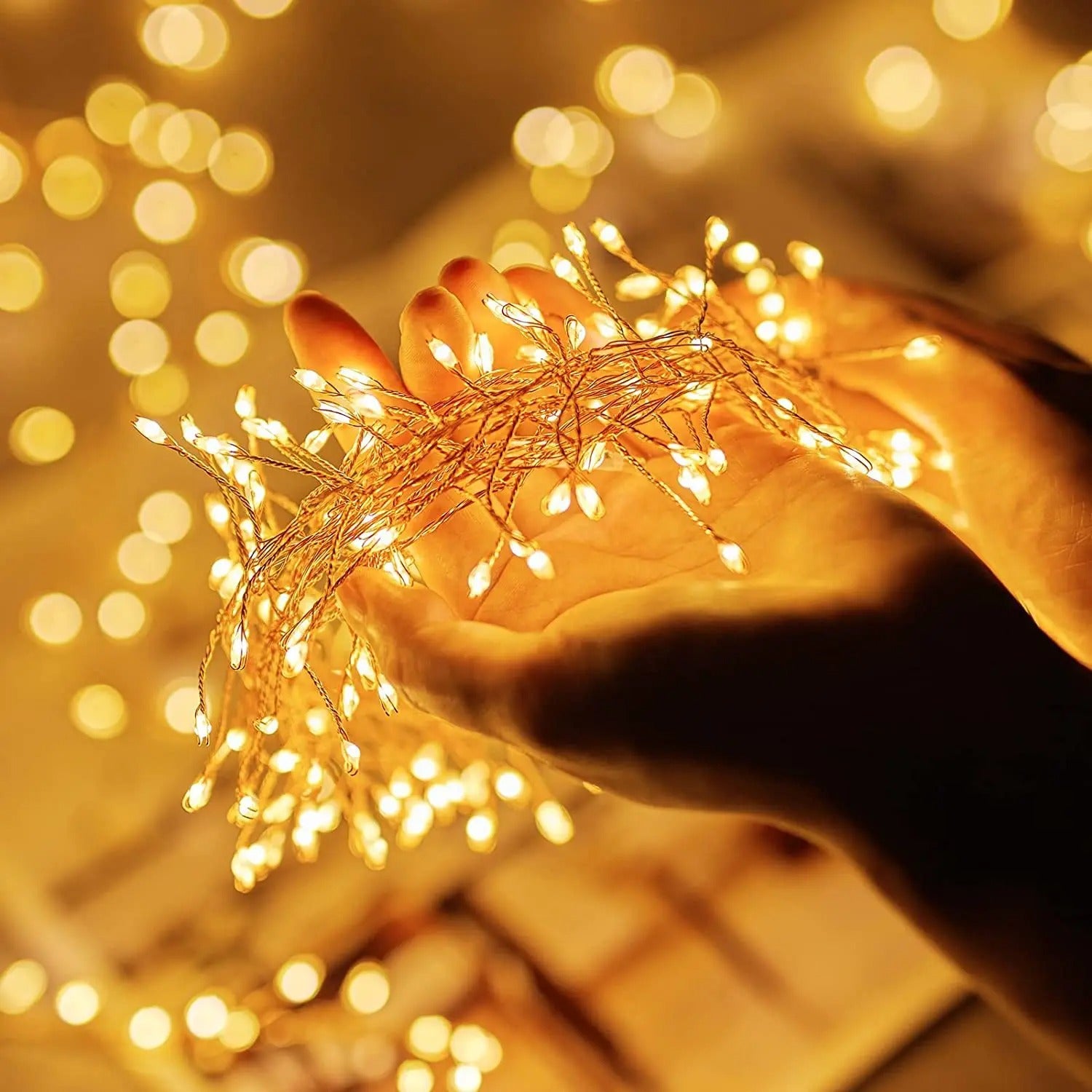 Hand holding a string of small lights with a warm, blurred light background