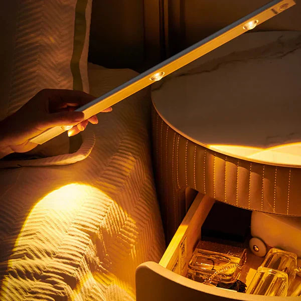 Person holding a light strip above a jewelry box with items inside, illuminated by the light.
