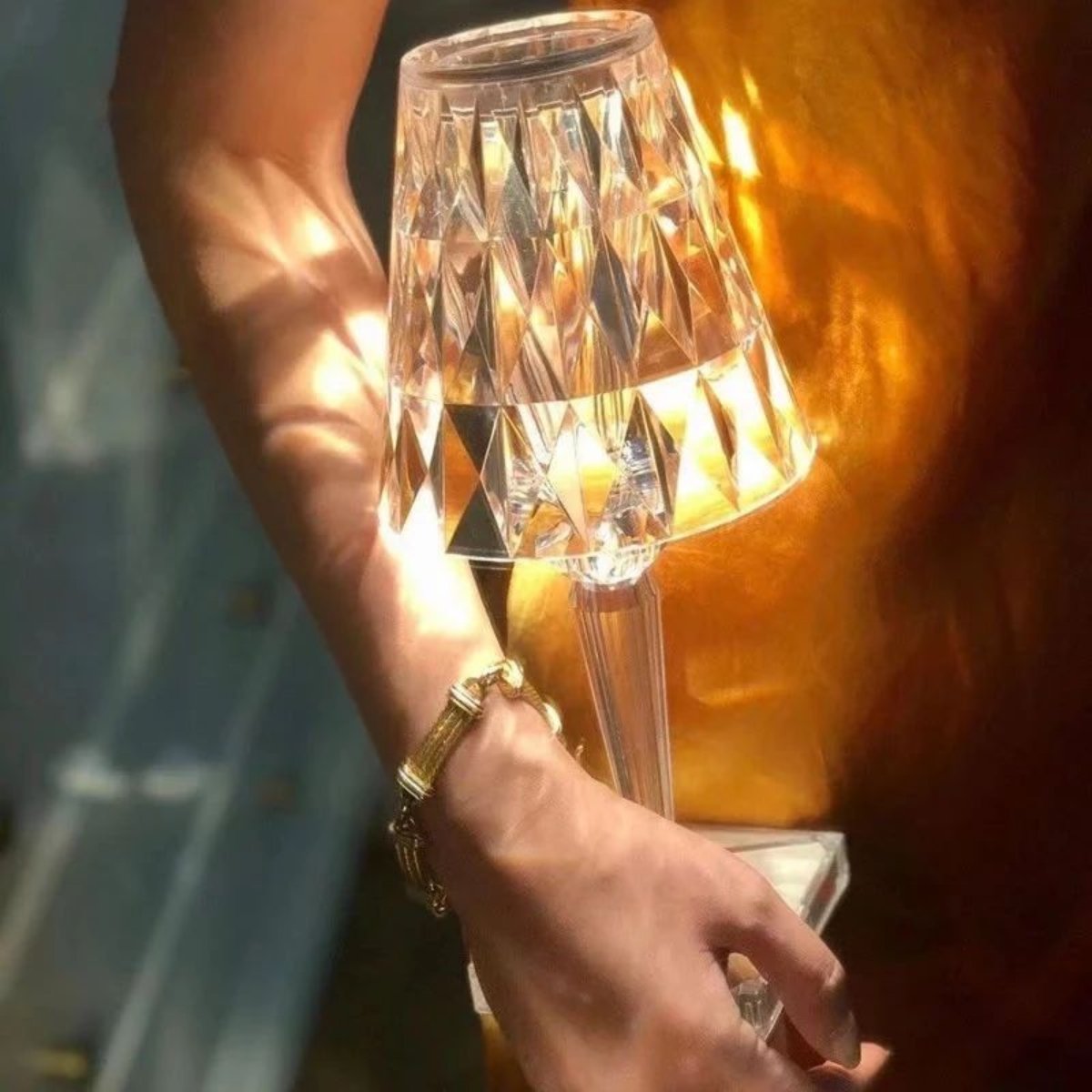 Hand holding a small, illuminated lamp with a textured shade against a blurred background