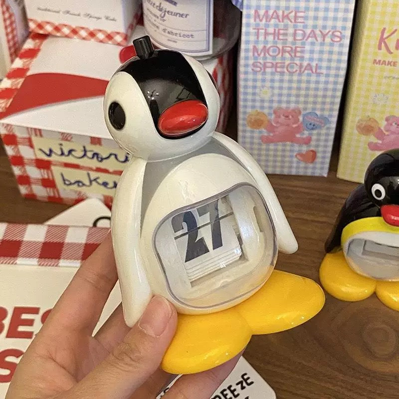 Penguin-shaped calendar held by a hand with a blurred background of boxes and products.