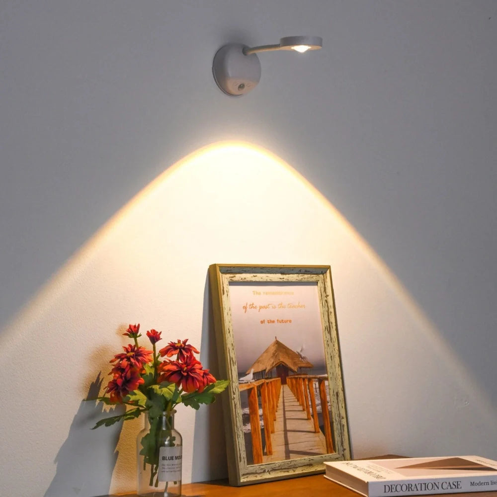Wall-mounted light fixture casting a warm glow on a framed picture and flowers on a table.