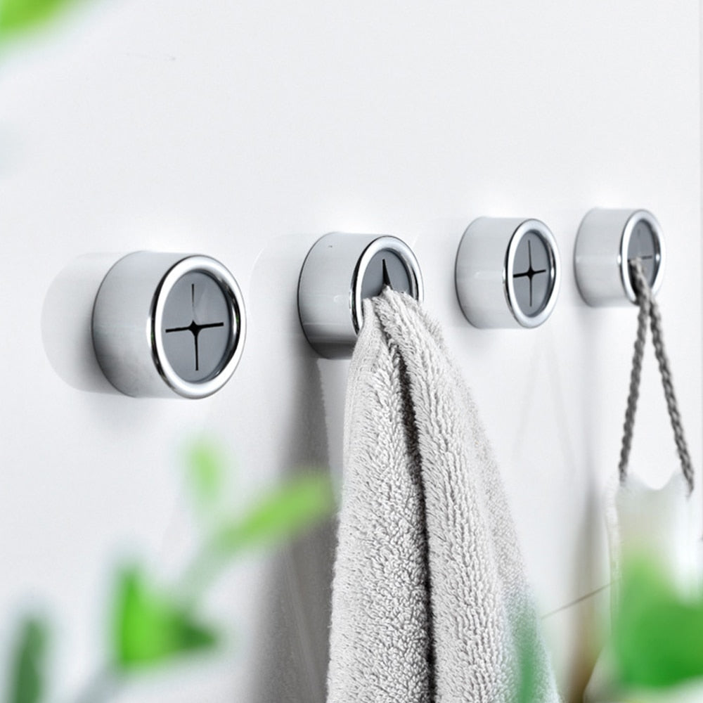 Set of four wall-mounted hooks with a towel hanging on one of them, against a light background.