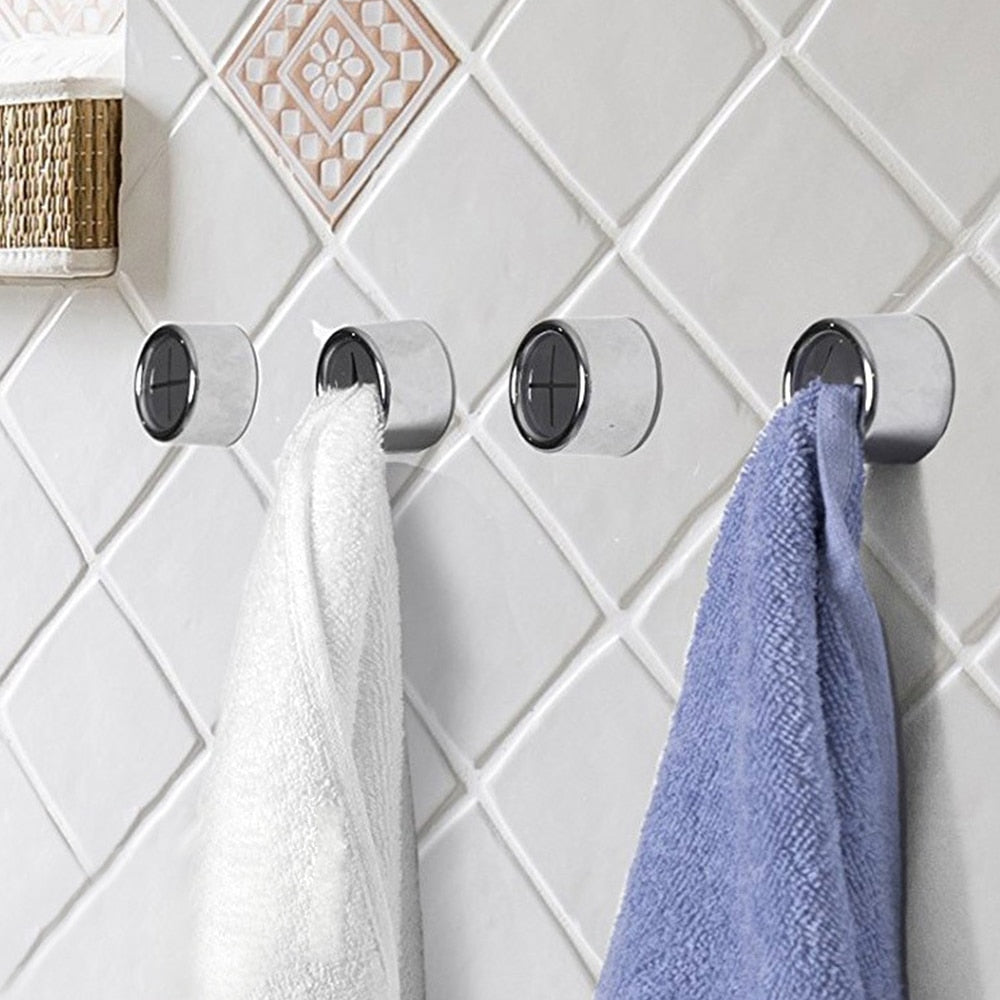 Four silver hooks on a tiled bathroom wall with white and blue towels hanging from them.