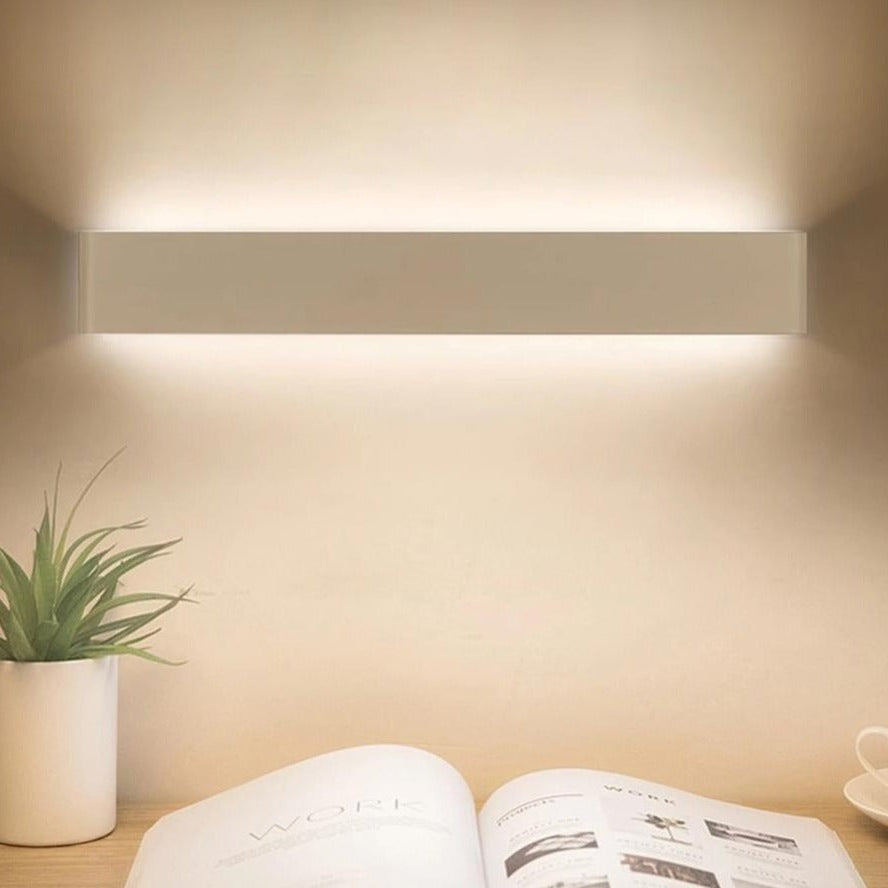 Wall-mounted light fixture casting a warm glow on a book and plant on a table.