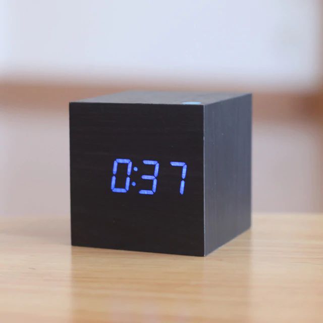 Black digital clock with blue LED display on a wooden surface