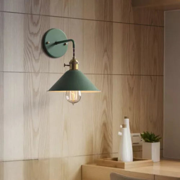 Green wall lamp on a wooden wall with a desk and plant in the background