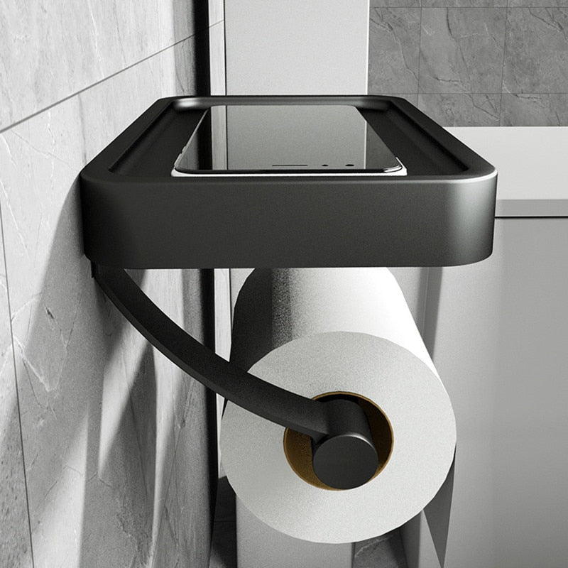 Black wall-mounted toilet paper holder with a roll of toilet paper on a tiled bathroom wall.