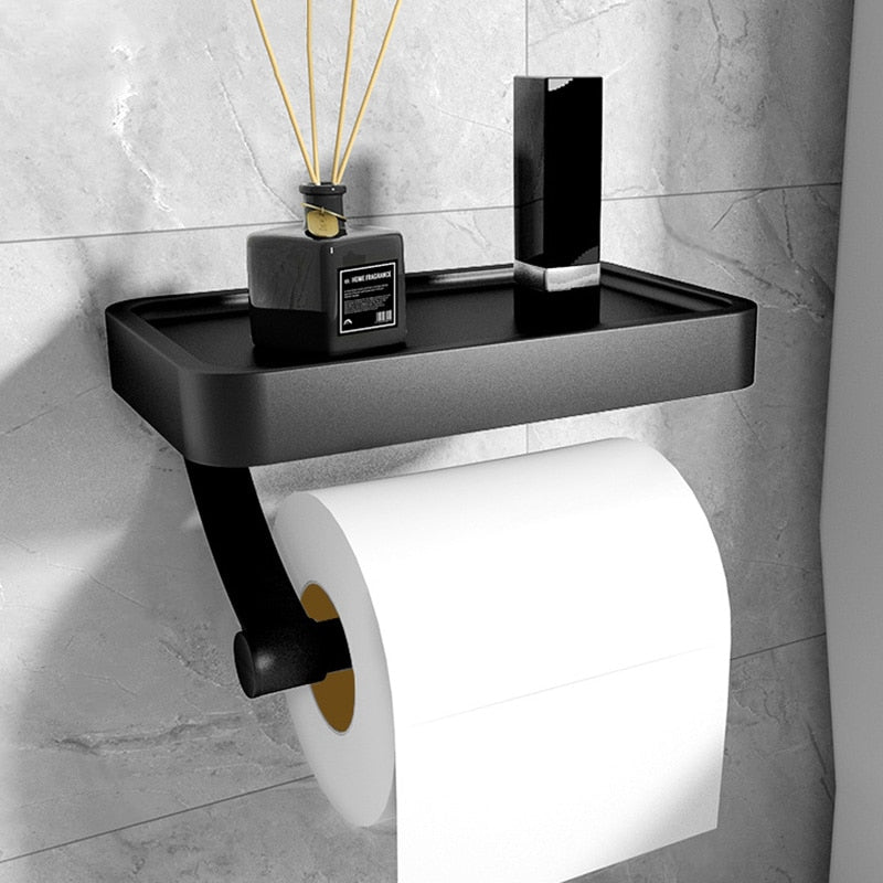 Black wall-mounted toilet paper holder with a roll of toilet paper on a tiled bathroom wall.