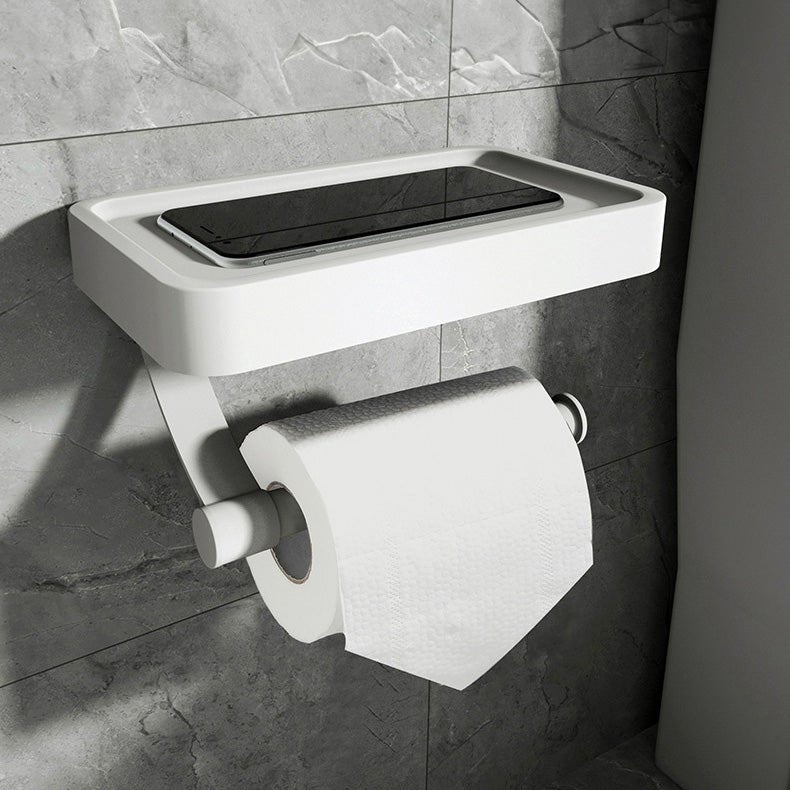 White wall-mounted toilet paper holder with a black rectangular object on a tiled bathroom wall.