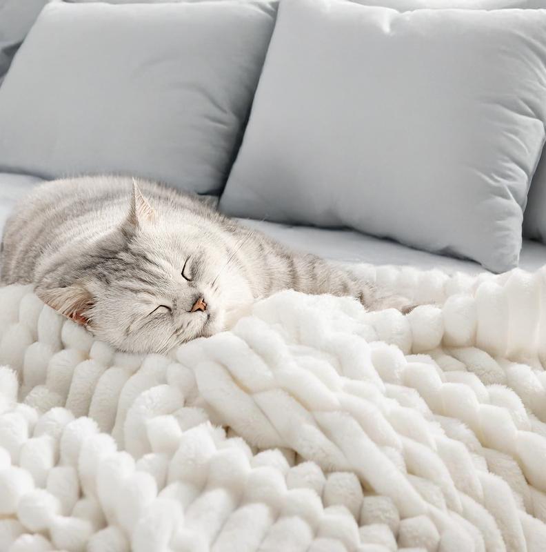 Cat sleeping on a fluffy white blanket with a gray couch in the background