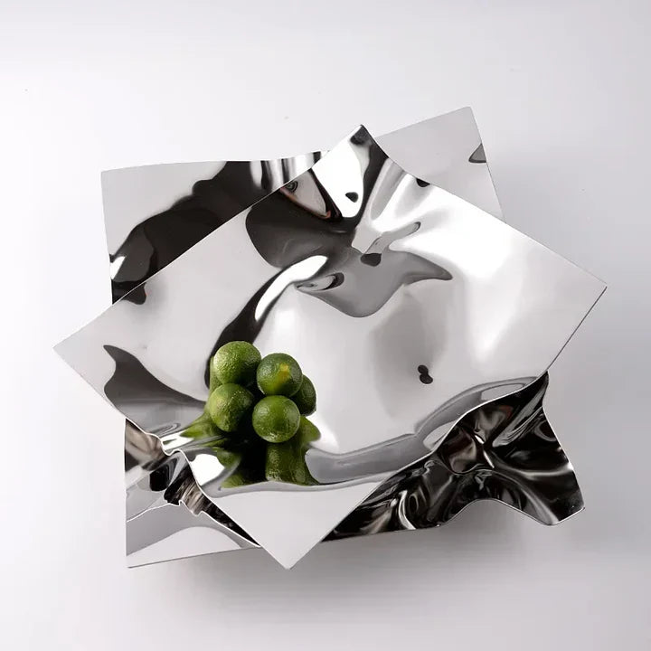 Silver decorative plate with a unique geometric design holding green apples on a white background